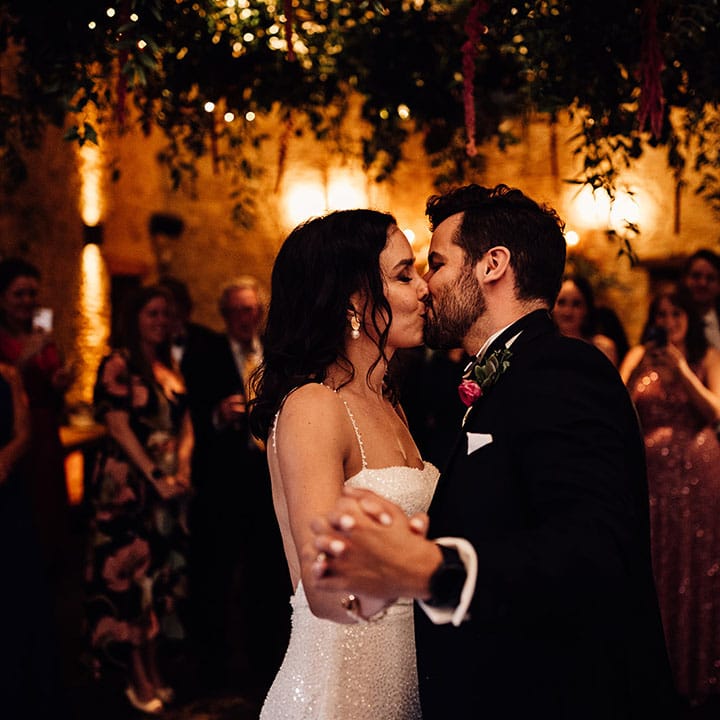 Wedding guests watch on as the bride and groom share their first dance together and kiss 