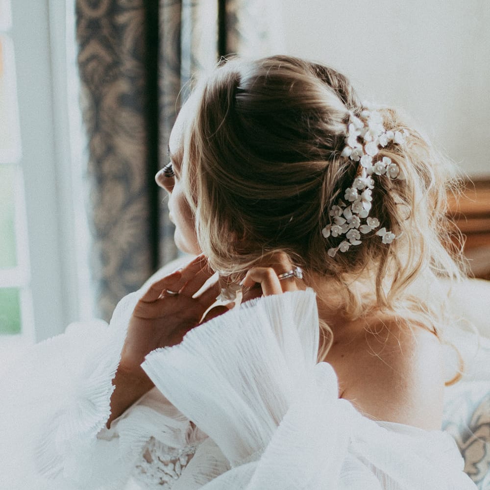 Bride in lace detailed wedding dress with long layered puff sleeves and roses hair clip with pearl details