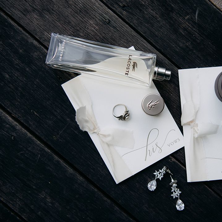 Minimalistic his and hers vows stationery with off white lace ribbon and calligraphy, wedding rings, Lacoste perfume, and diamond drop earrings