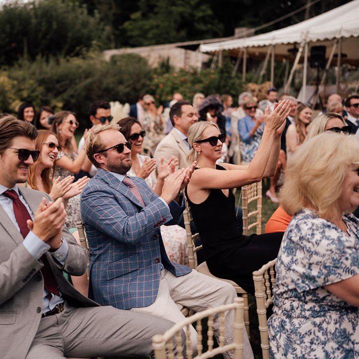 Wedding guests seated at the outdoor wedding ceremony starts applauding for the bride and groom 