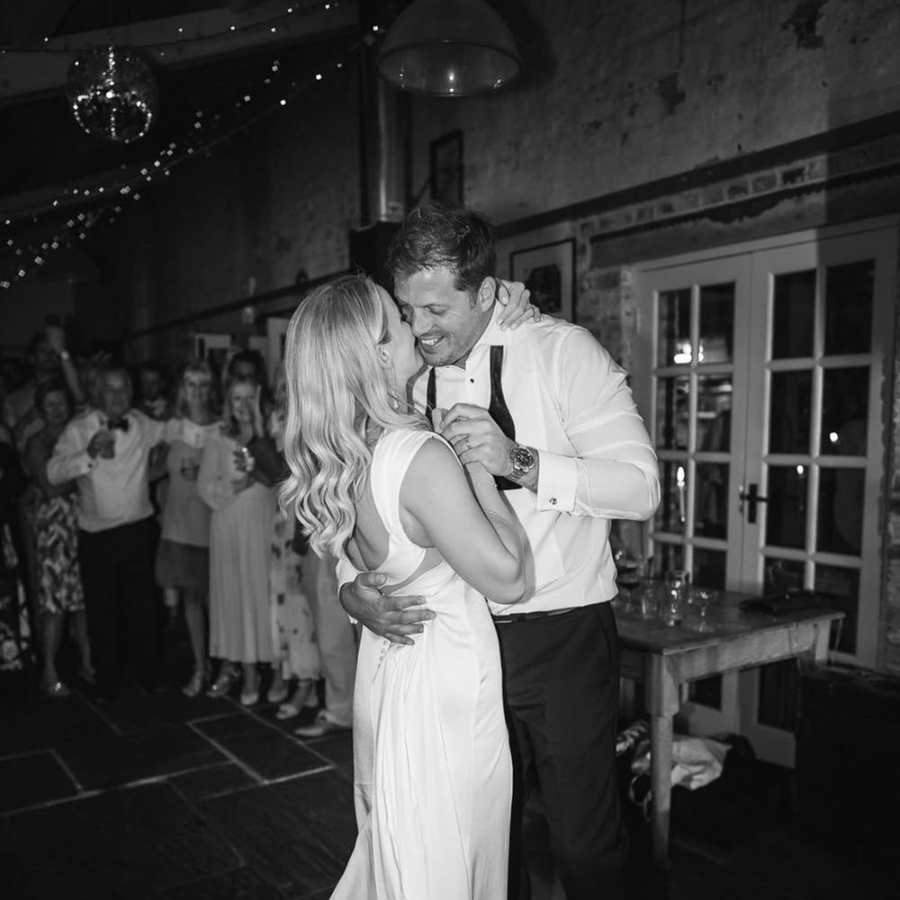 Bride in a white satin wedding dress sharing her first dance with the groom wearing his bow tie undone 