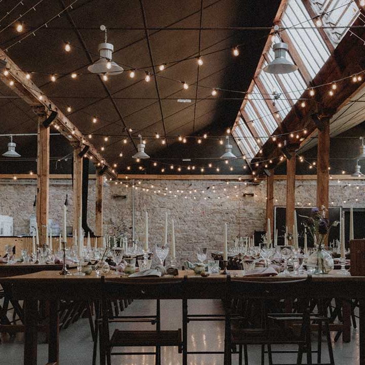 Industrial styled reception venue complete with festoon lighting and wooden banquet tables with DIY florals 