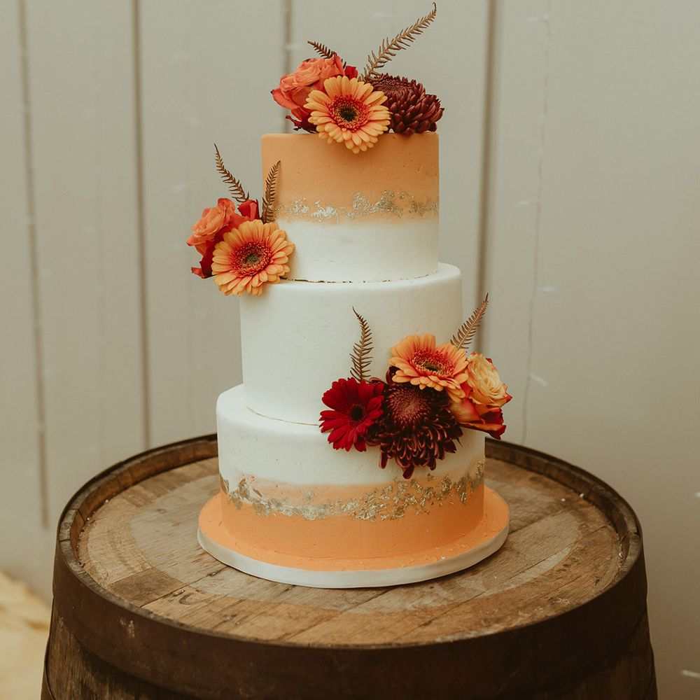 Three tier white and orange ombre iced wedding cake with gold flakes and red and orange chrysanthemums and roses 