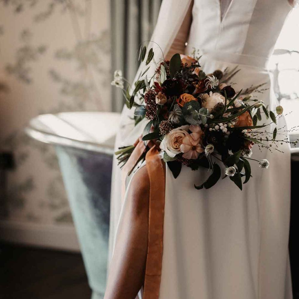 Bride in ivory wedding dress with front leg slit holding mixed neutral bouquet, wearing strapless wedding high heels with large white bow 