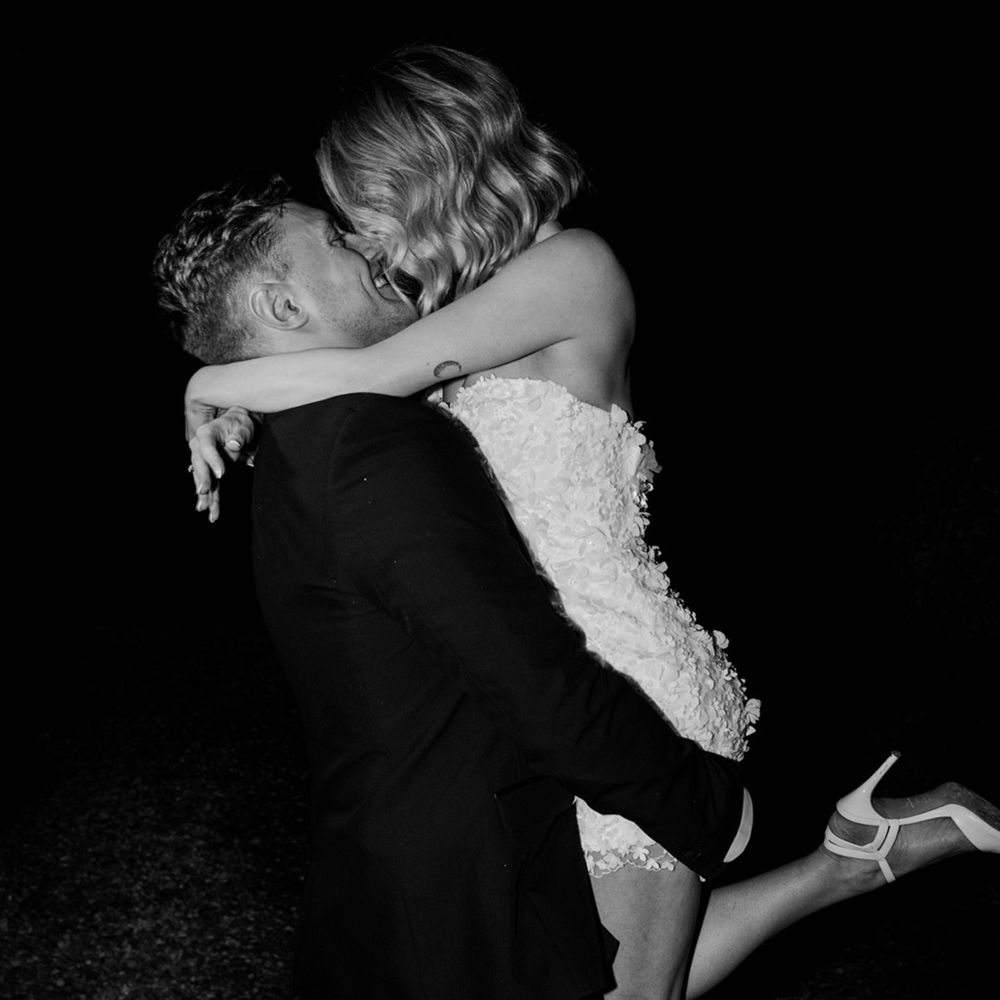 The groom in black tie lifts the bride up for a kiss wearing a short wedding dress for the wedding reception at Wyresdale Park 