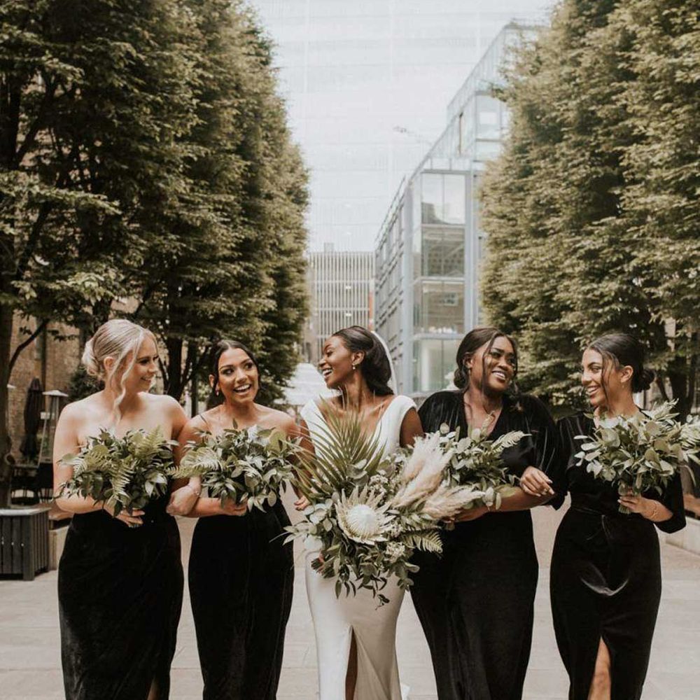 Bride in deep plunge neckline wedding dress walking with bridesmaids in mismatched black bridesmaid dresses 