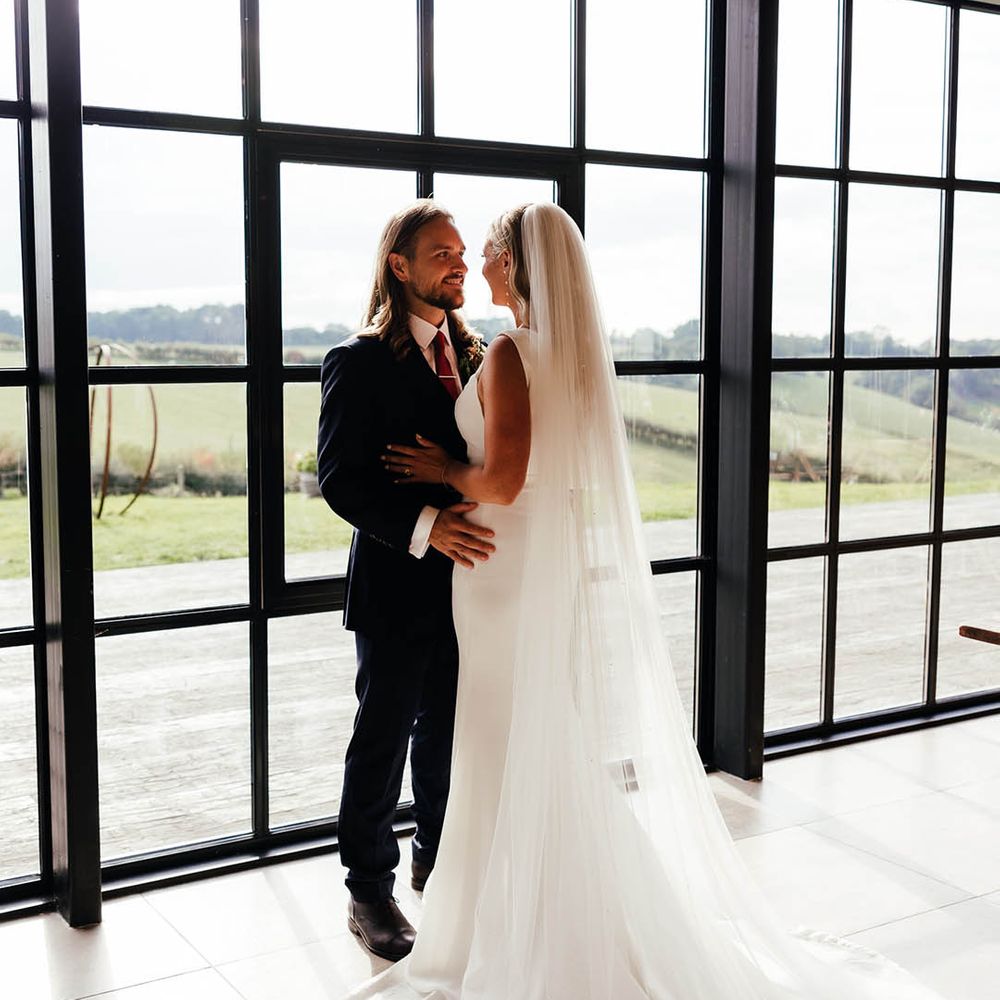Bride and groom pose in front of the iconic windows at Botley Hill Barn in Surrey 