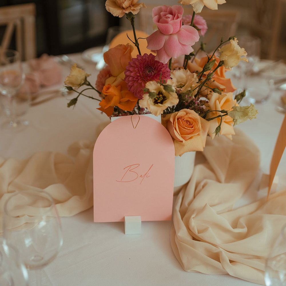 pink and yellow centrepiece flowers and arched wedding table sign 