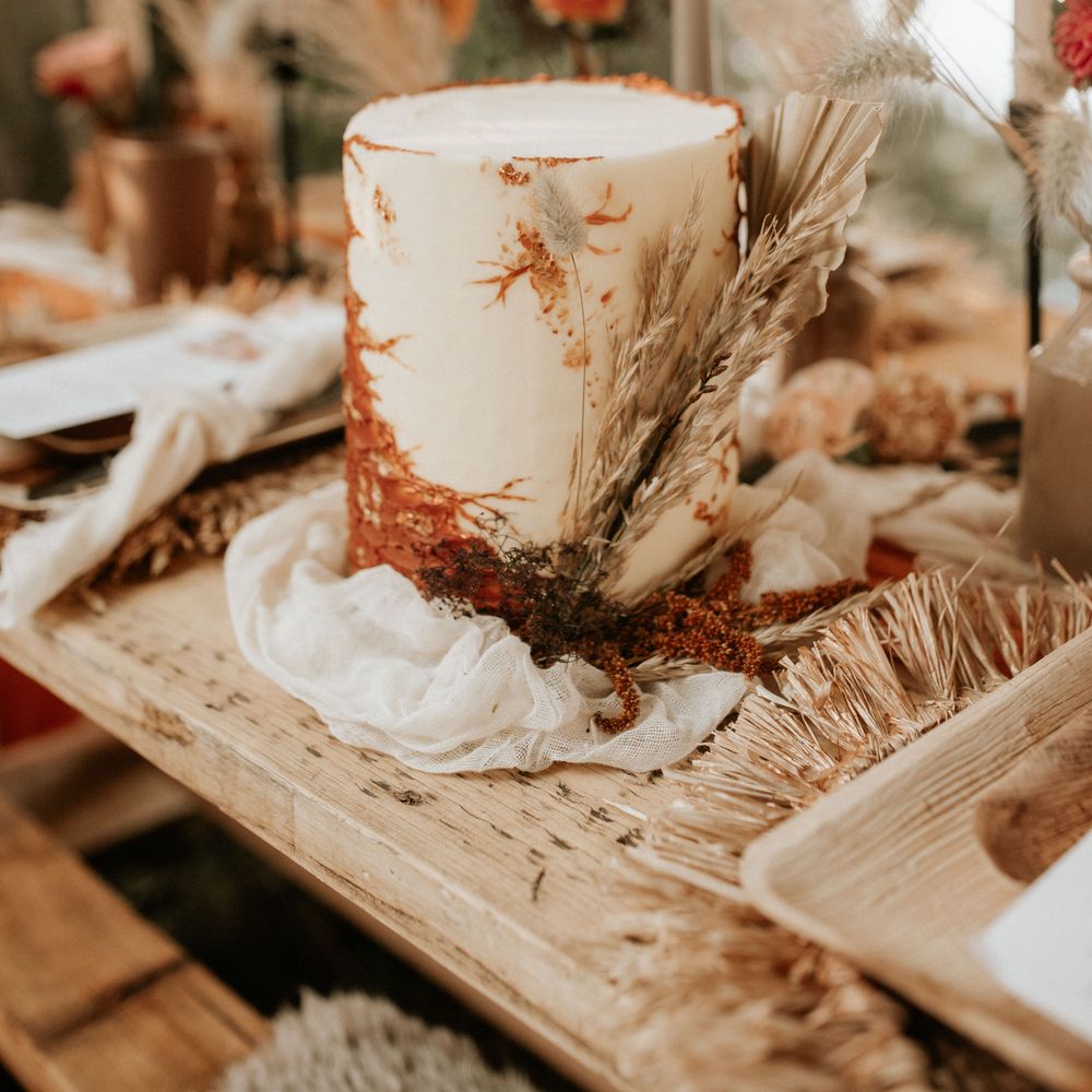 White and burnt orange wedding cake with gold leaf decoration on wooden table