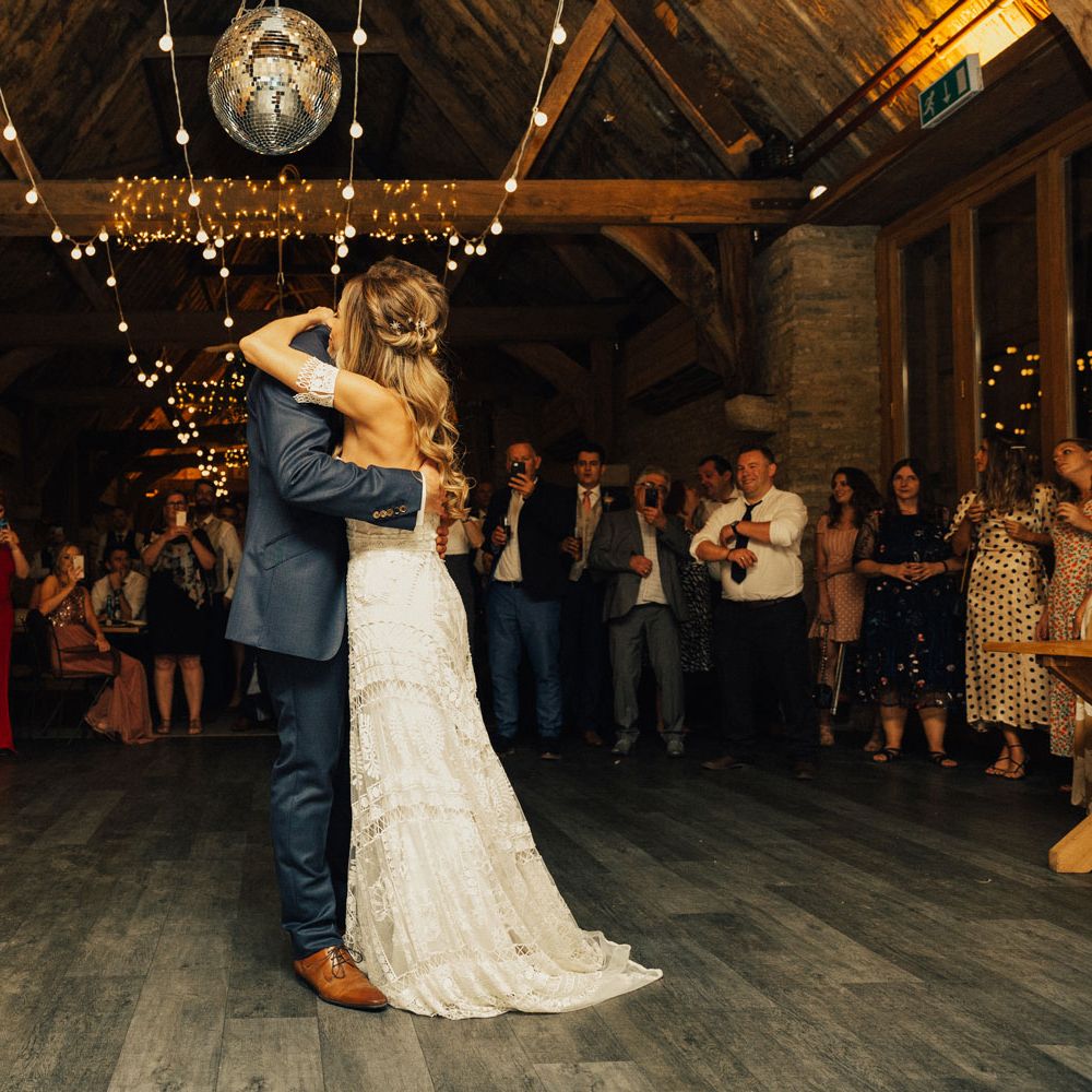 Bride in boho Rue De Seine Dress and Groom in Navy suit have first dance under disco ball and fairy lights