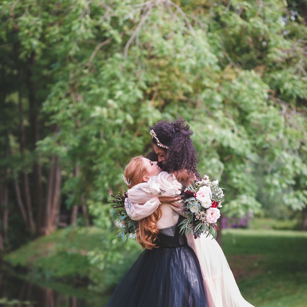 Two brides embracing at autism marriage diverse wedding inspiration. Brides wear coloured wedding dresses and pretty hair accessories