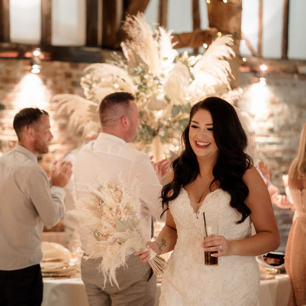 Beautiful bride walking through the barn wedding reception holding a dried flower wedding bouquet 