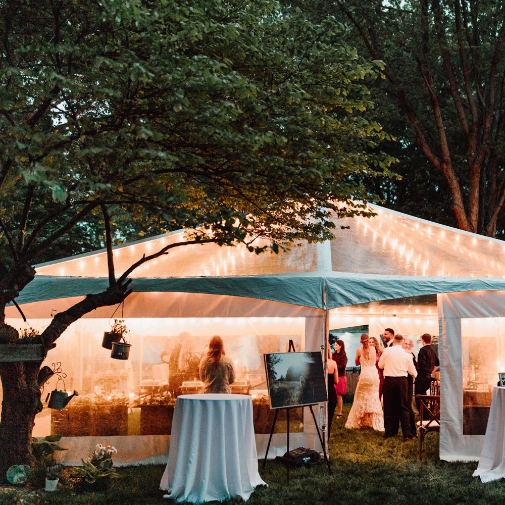 Exterior of white fairy lit marquee full of wedding guests for backyard wedding
