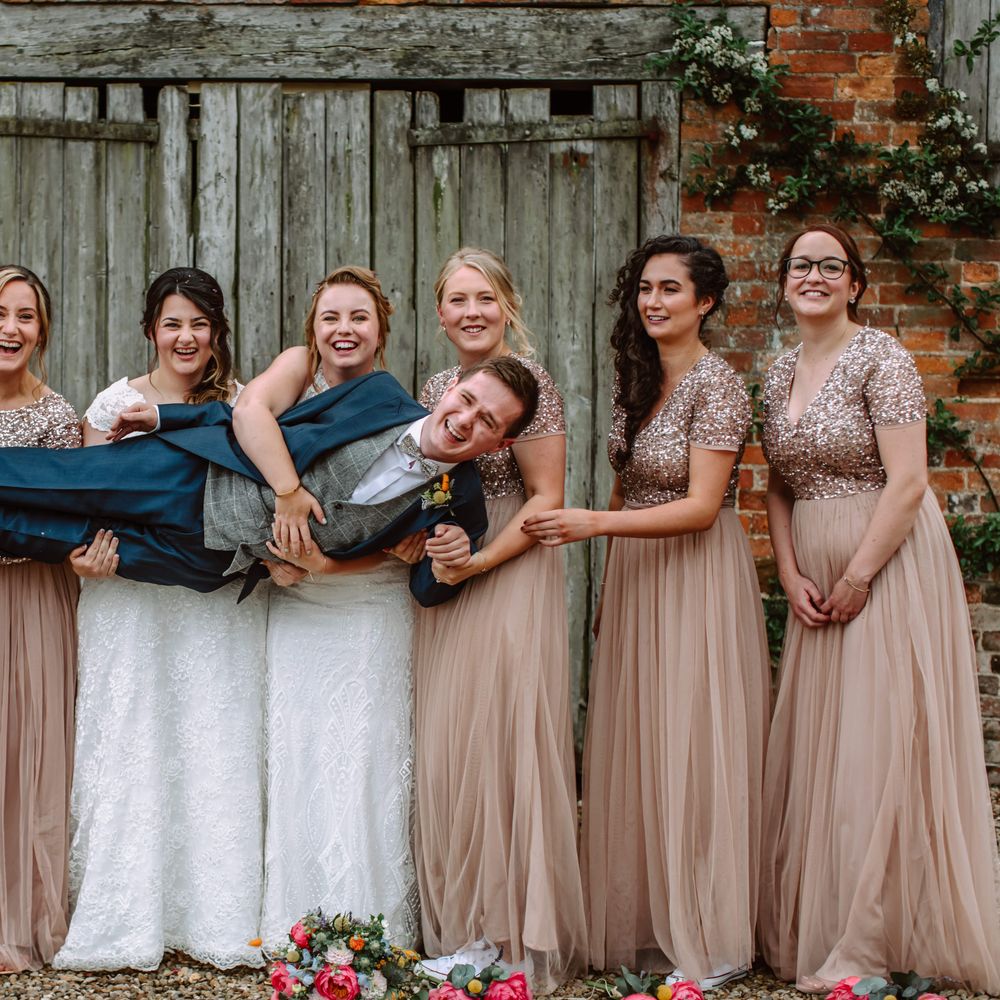 Wedding guest is held up by brides and bridesmaids who were pale pink gowns with sequinned tops