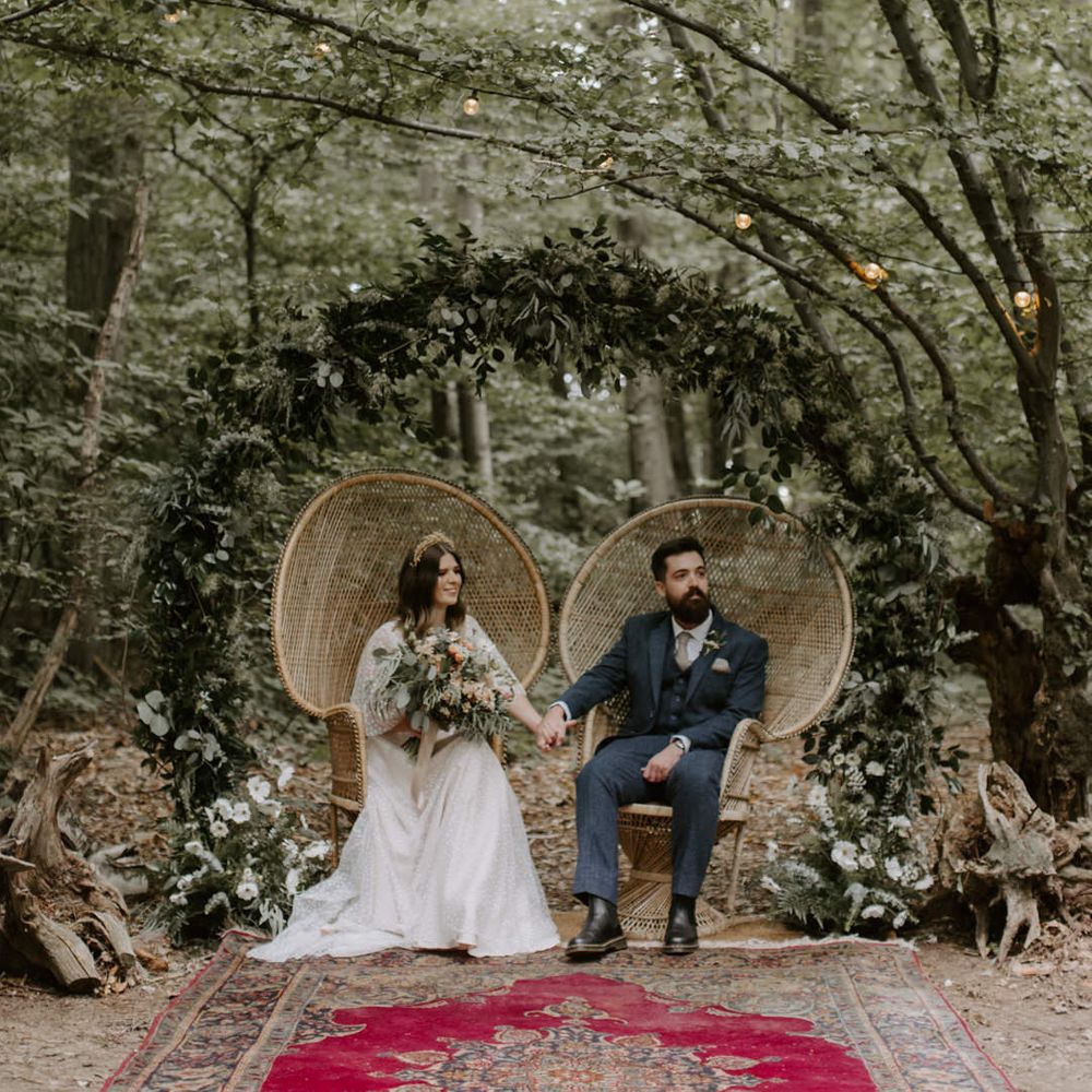 Bride & groom hold hands whilst sitting in sweetheart chairs