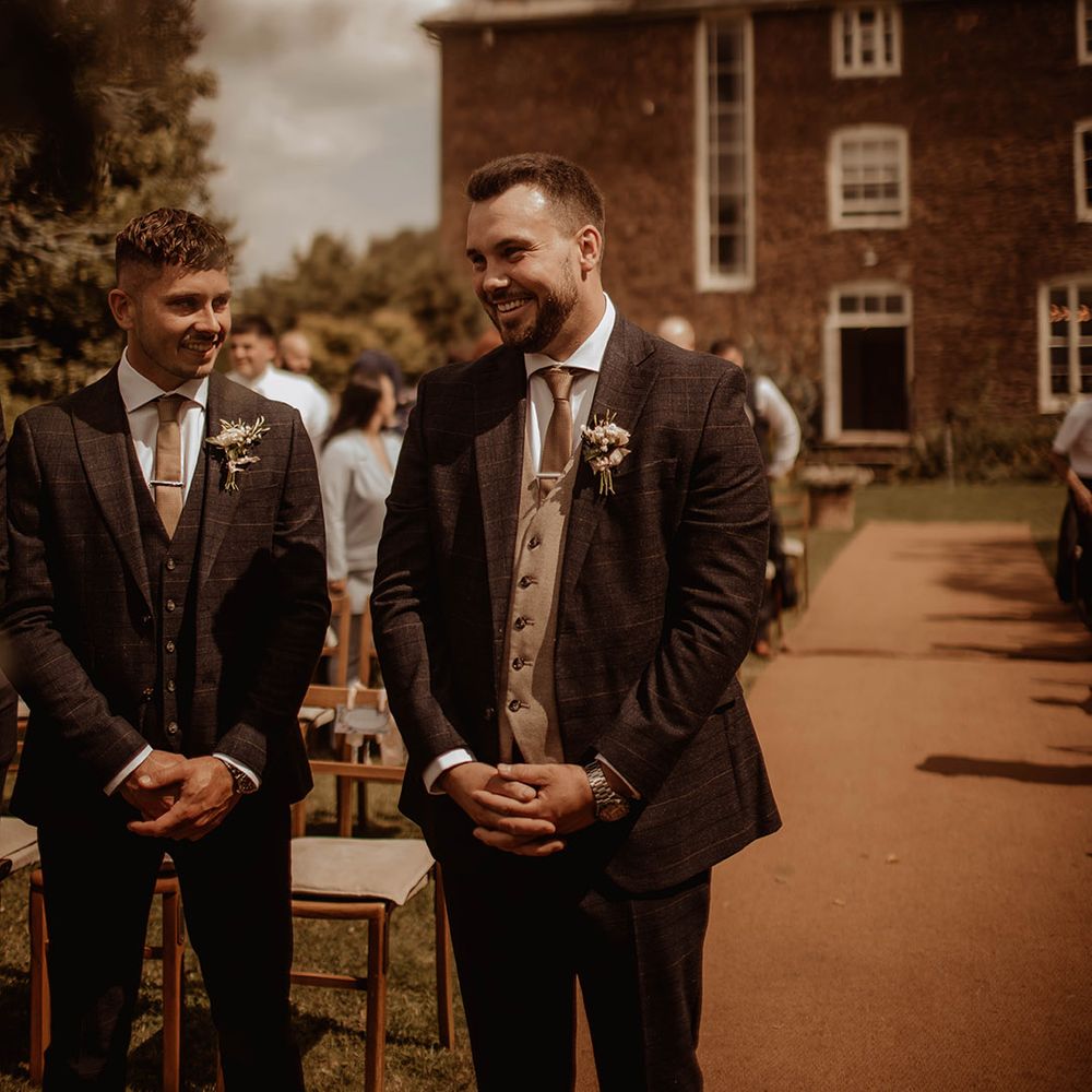 groom and best man in check suits at the altar of an outdoor wedding at Dewsall Court