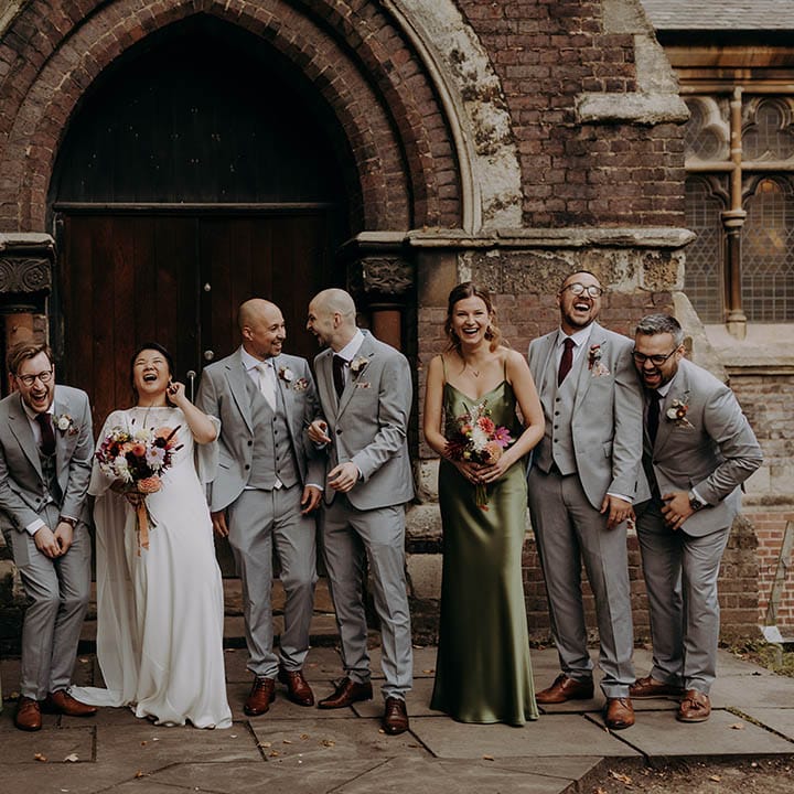 Bride & groom stand with their wedding party, as bridesmaids wear sleek satin olive green bridesmaids gowns and grooms wear grey three piece suits  | Irene Yap Photography
