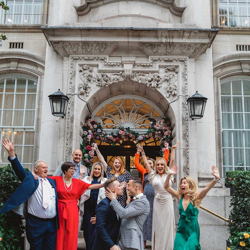 Grooms stand in front of Chelsea Old Town Hall on their wedding day