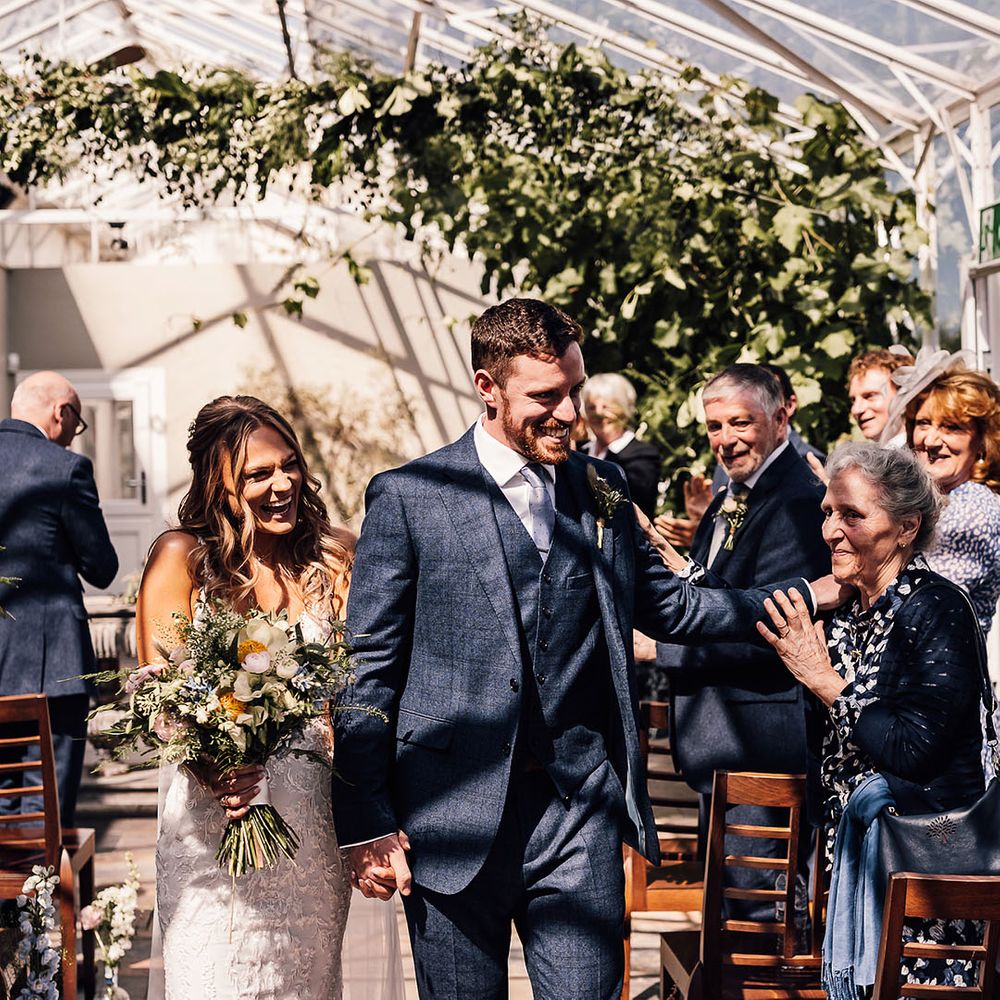 Groom in blue three piece suit and light blue tie walks back down the aisle with the bride as a married couple 
