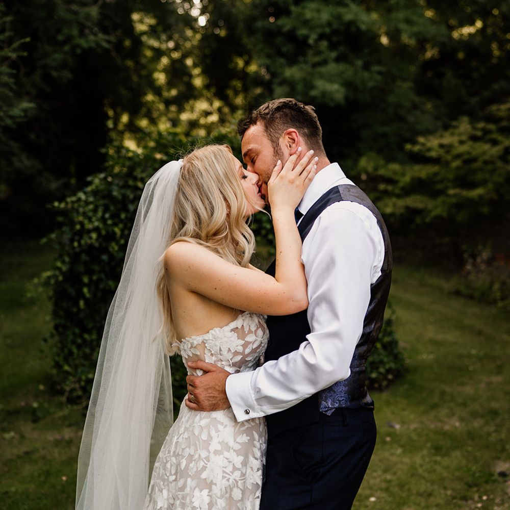 Bride in a Lillian West wedding dress reaches up and kisses the groom 