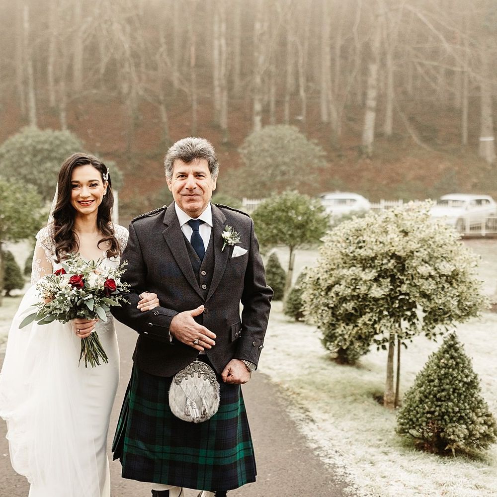 Bride walks with her father outdoors surrounded by snow covered grass and trees in Scotland 