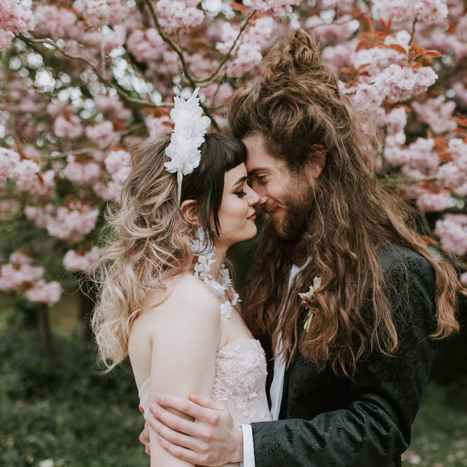Groom with long hair in a tuxedo kissing his bride in a pink strapless wedding dress