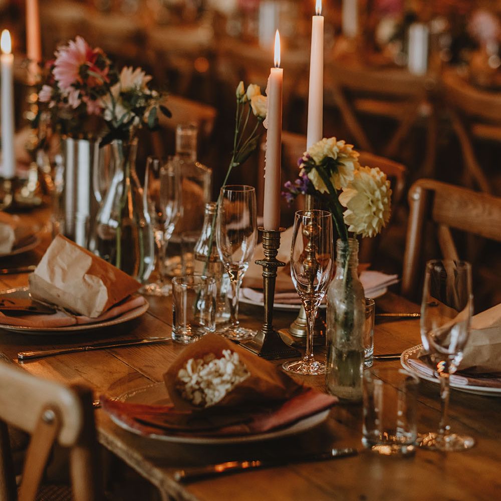 Pale pink candles in vintage brass candle holders beside small floral arrangements on wooden tables 