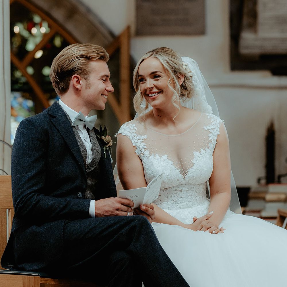 Groom in a blue tweed suit with a grey waistcoat sitting with the bride in a princess wedding dress and veil sitting for their wedding ceremony 