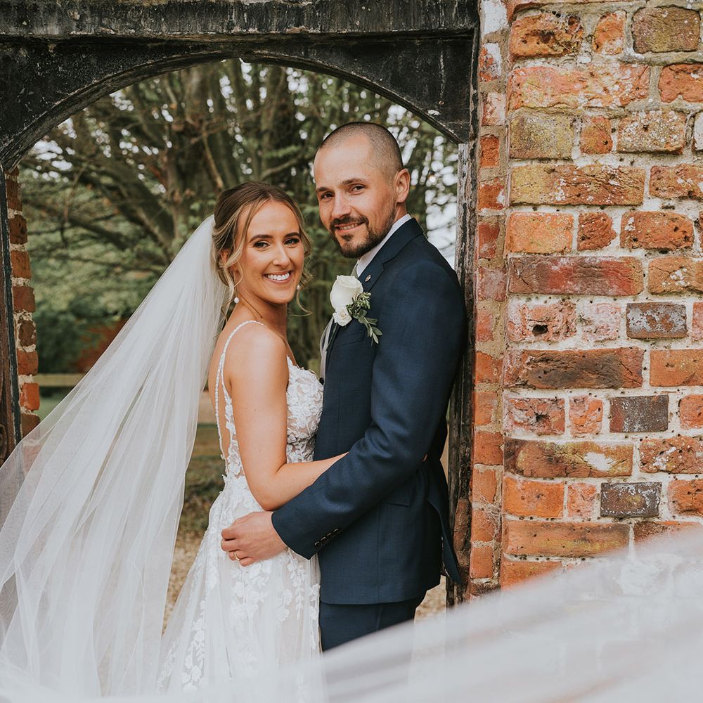 Bride with a long wedding veil and low back wedding dress with the groom in a dark blue three piece suit 