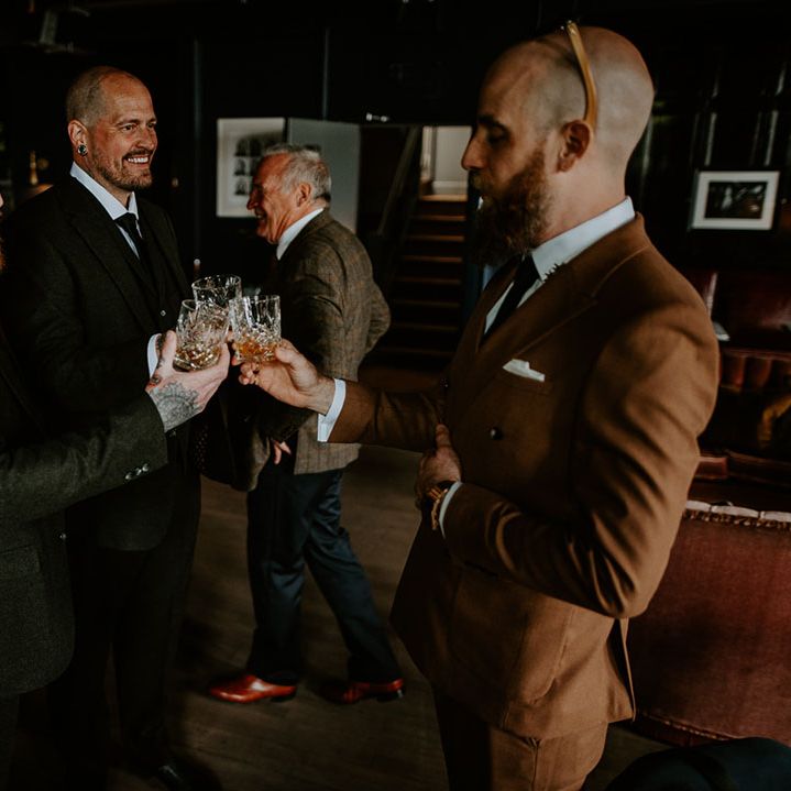 Groom in retro brown suit stands with wedding guests at bar during reception 
