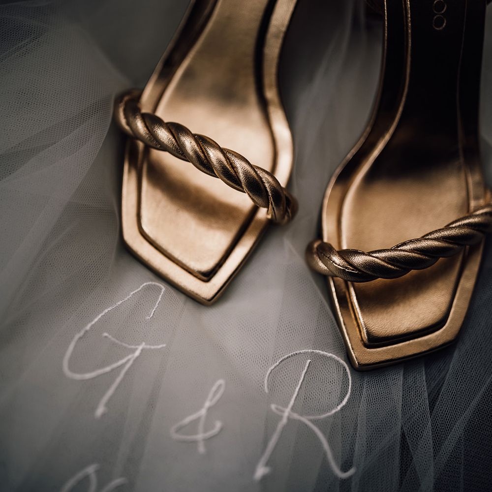 Gold metallic Jimmy Choo wedding shoes resting on top of a veil with personalised embroidered initials and wedding date 