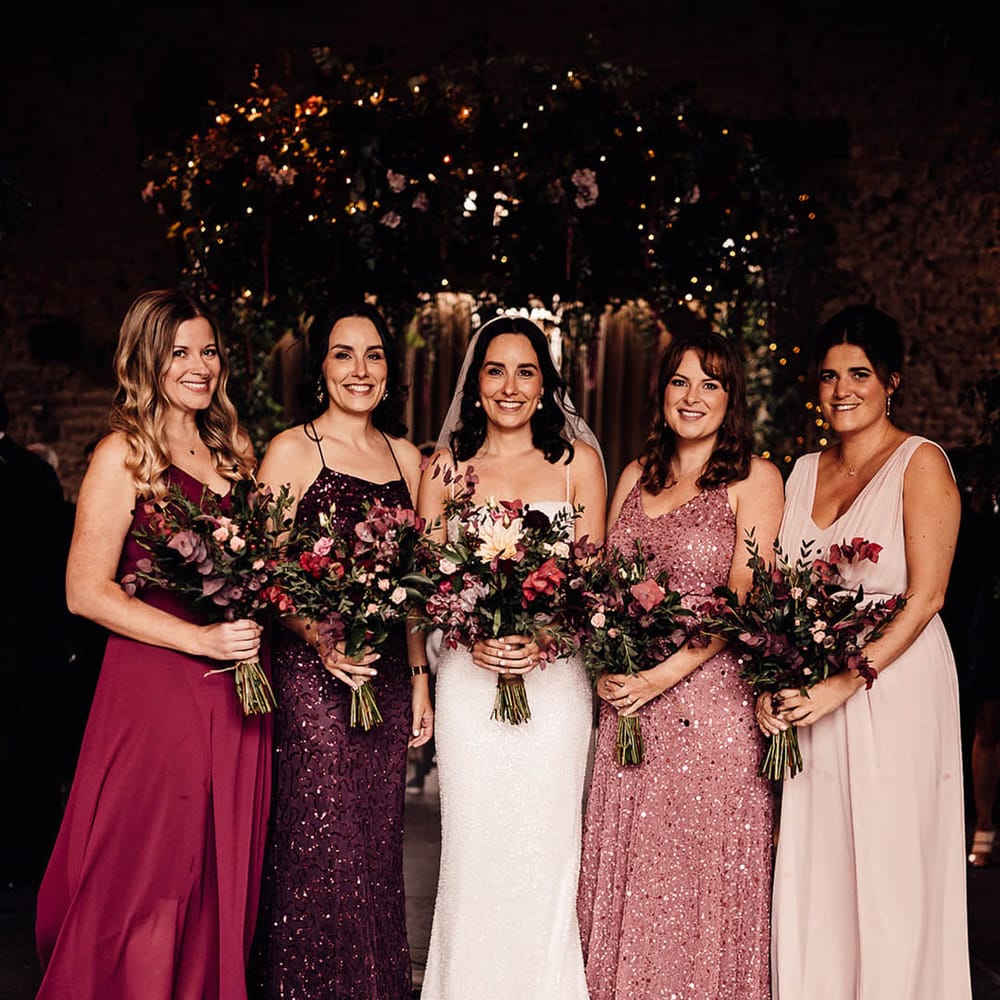 Smiling bride with bridesmaids in mismatched sparkly bridesmaid dresses in shades of pinks and purples 
