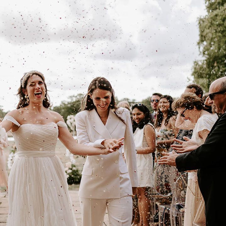 The brides walk holding hands together as they have their confetti moment 