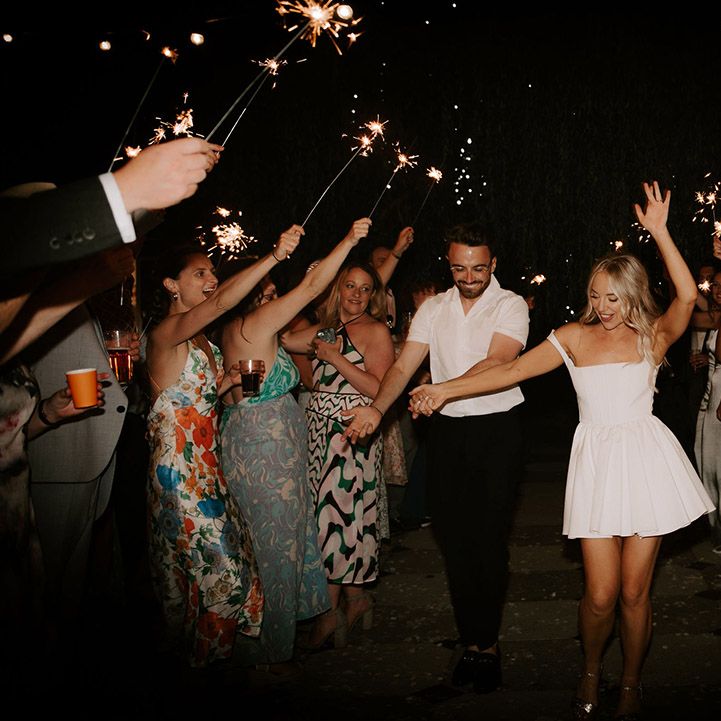 Bride changed into short white wedding dress walking with the groom in a white shirt have a sparkler send off 
