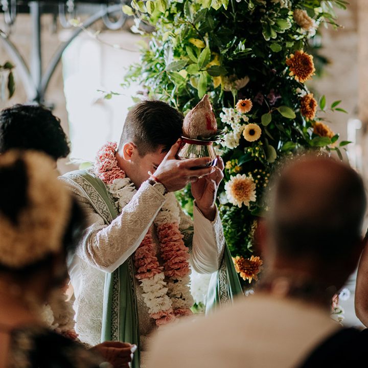 Grooms stand beneath floral archway at The Tithe Barn Bolton Abbey during Hindu & Punjabi wedding ceremony 