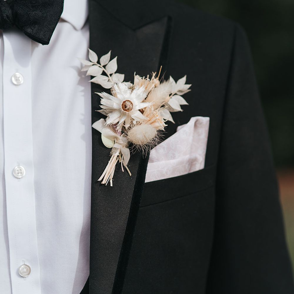 Groom in black tie with a white pocket square and white dried flower buttonhole 