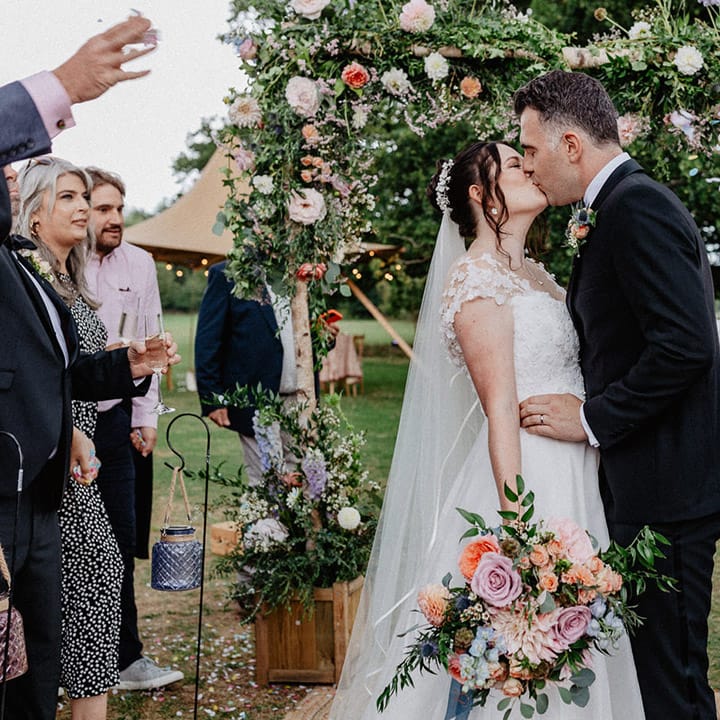 Colourful spring wedding flower arch at Culden Faw Estate with the bride and groom sharing a kiss 