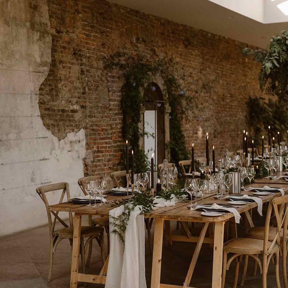 Neutral rustic wedding tablescape with white cloth table runners, foliage table runners and black tapered candles 