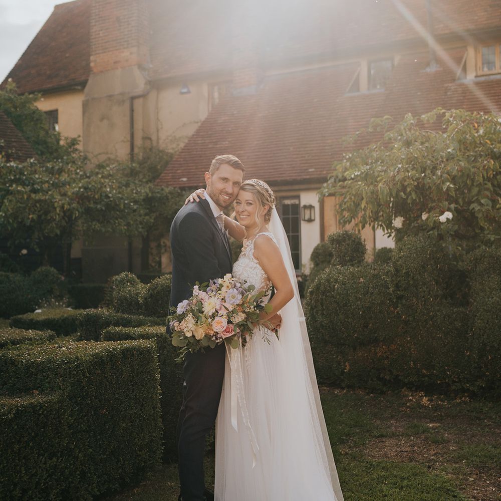 Groom in navy suit embracing the bride in lace and tulle wedding dress during golden hour 