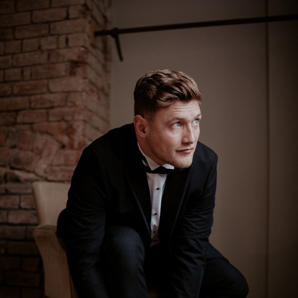 The groom gets ready for the big day wearing a classic black tuxedo putting on shiny black groom shoes 