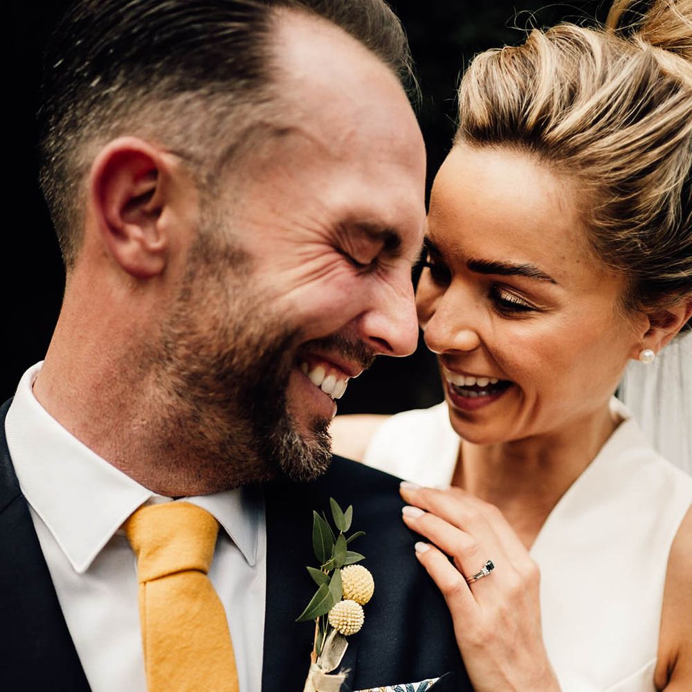 Navy groom suit with yellow tie and tie clip with yellow floral buttonhole and bride in deep plunging neckline wedding dress