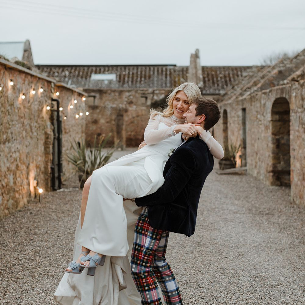Groom in tartan trousers spins the bride around who wear blue Loeffler Randall wedding shoes 