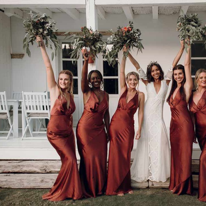 Bride wearing boho lace wedding dress standing with bridesmaids in burnt orange halterneck bridesmaid dresses 