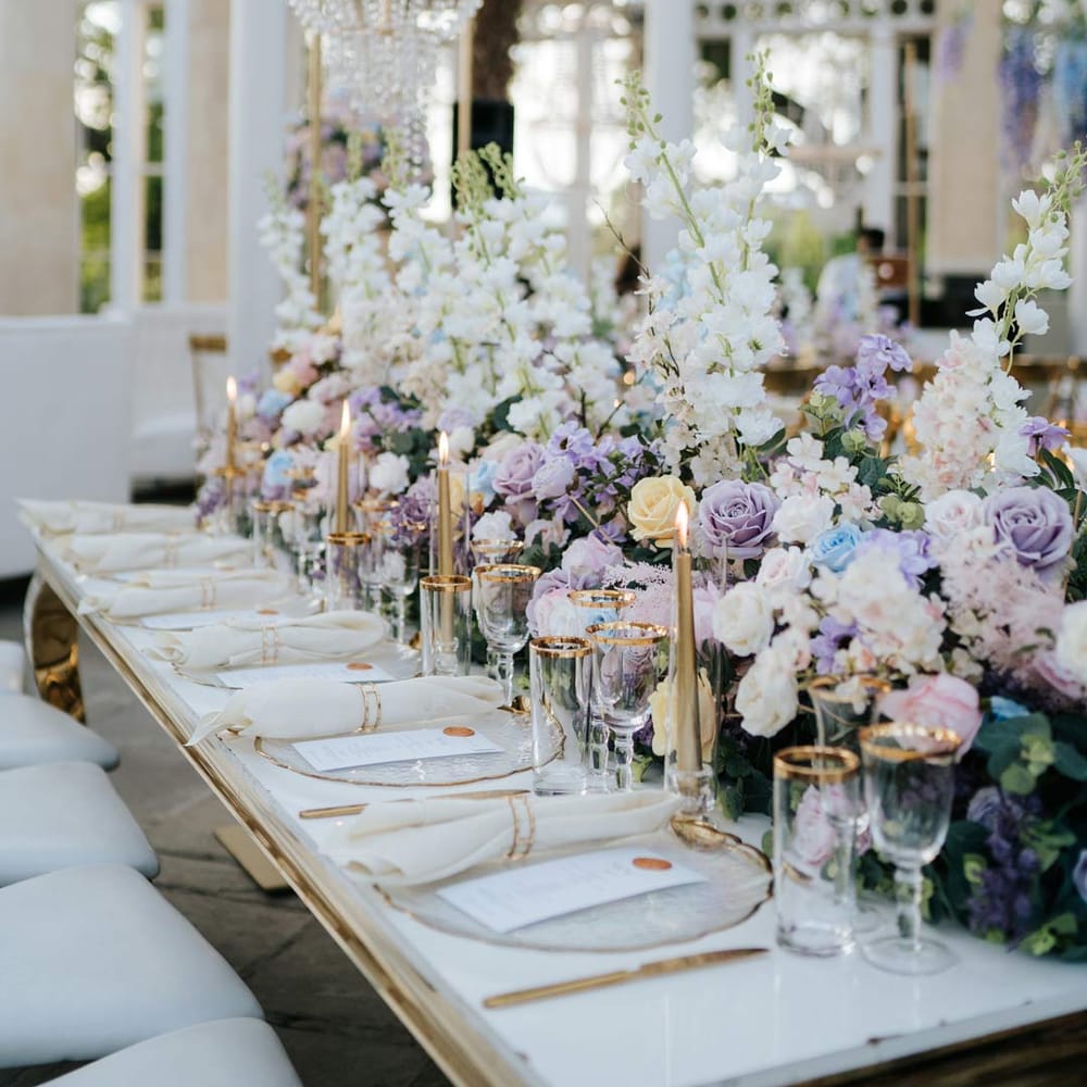 Syon Park wedding venue reception room with gold chairs, botanical tablescapes with large pastel flower centrepieces, gold tapered candles, gold rimmed tableware and suspended pastel foliage decor 