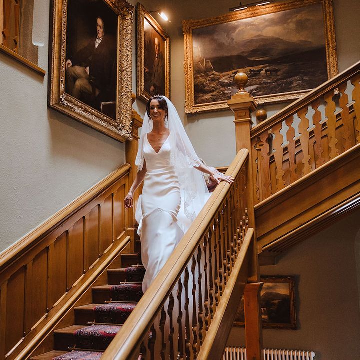 Bride in satin slip wedding dress walking down the stairs to the wedding venue 