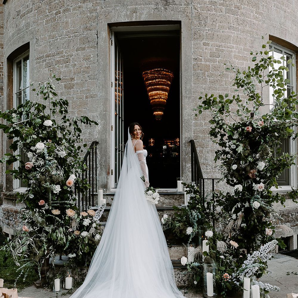 Bride wearing cathedral length veil at chic and elegant wedding with white flower column decorations 