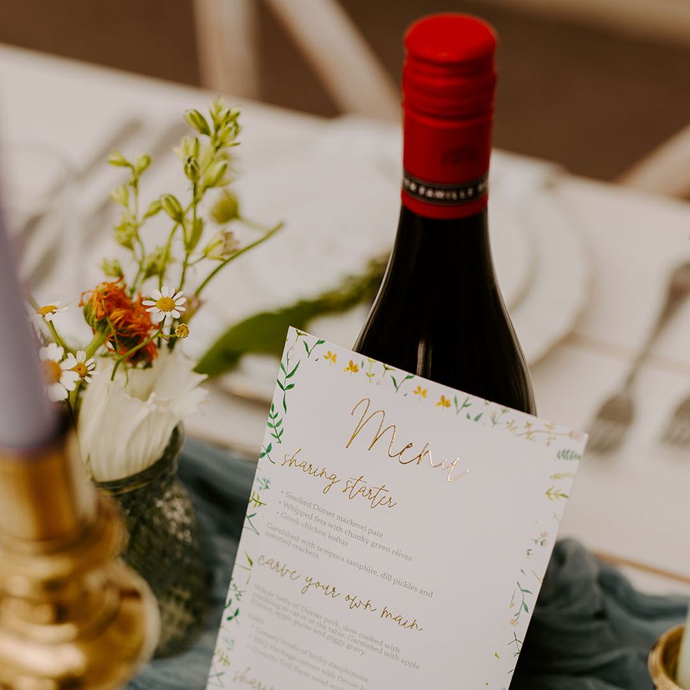 DIY wedding menu with gold foil leaning against red wine bottle 