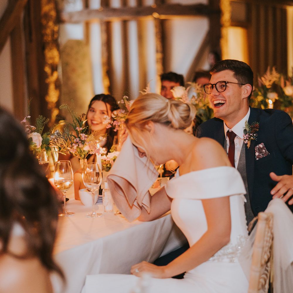 Bride & groom laugh with wedding party during speeches