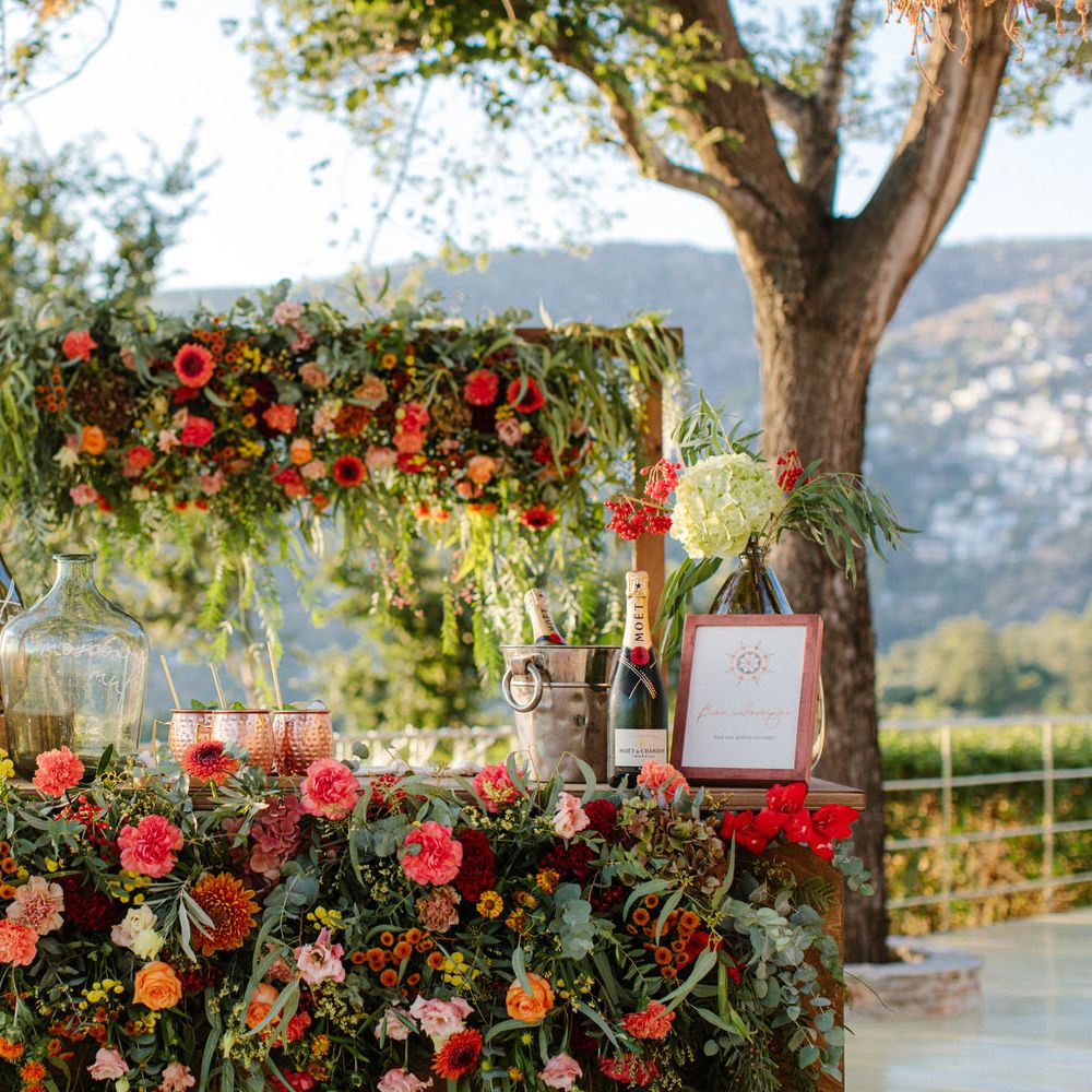 An outdoor cocktail bar covered in flowers, with prosecco, champagne and cocktails