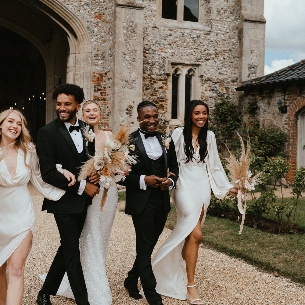 Stylish wedding party walking arm in arm along Pentney Abbey's driveway together 